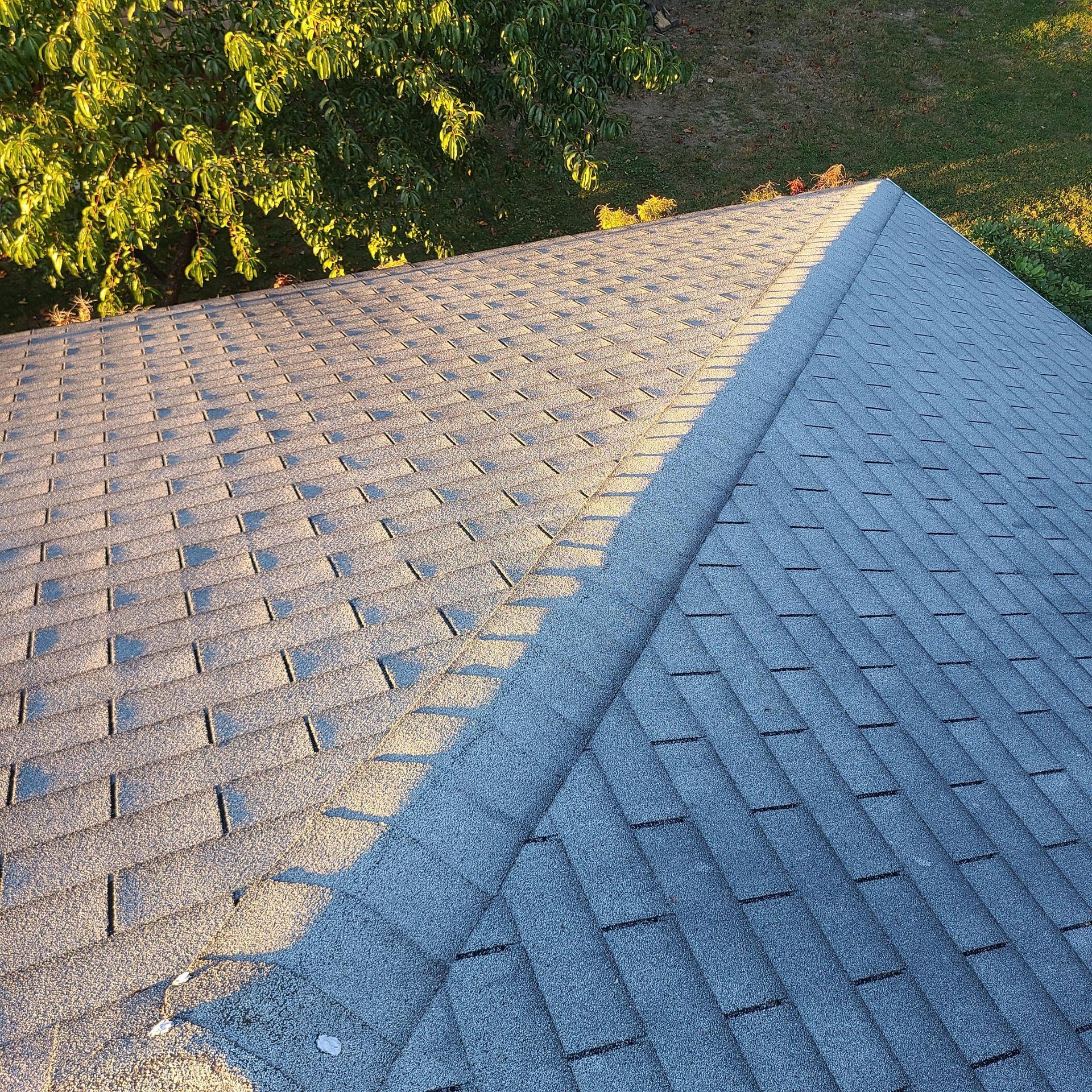 Overhead view of an asphalt shingle roof. The roof is gray and textured with a central ridge.