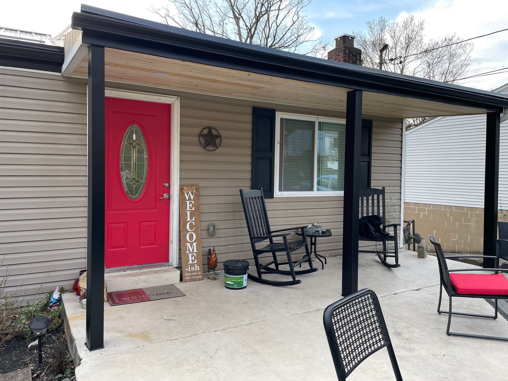 House with red door and black awning; porch with rocking chairs and table.
