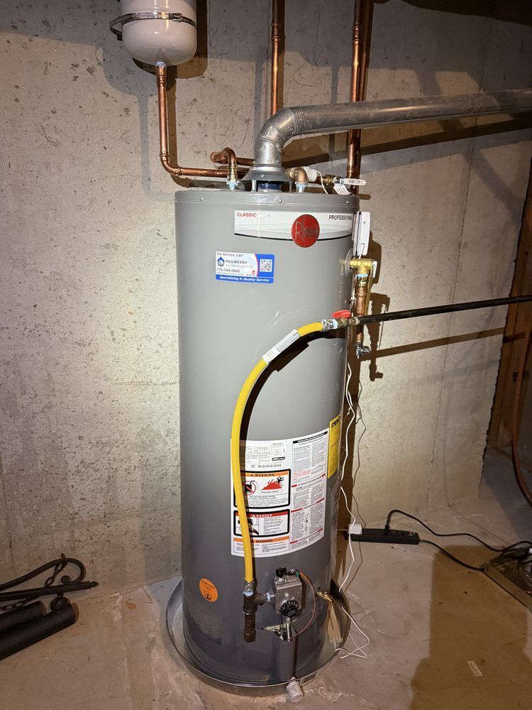Gray water heater with pipes and yellow hose in a basement utility area