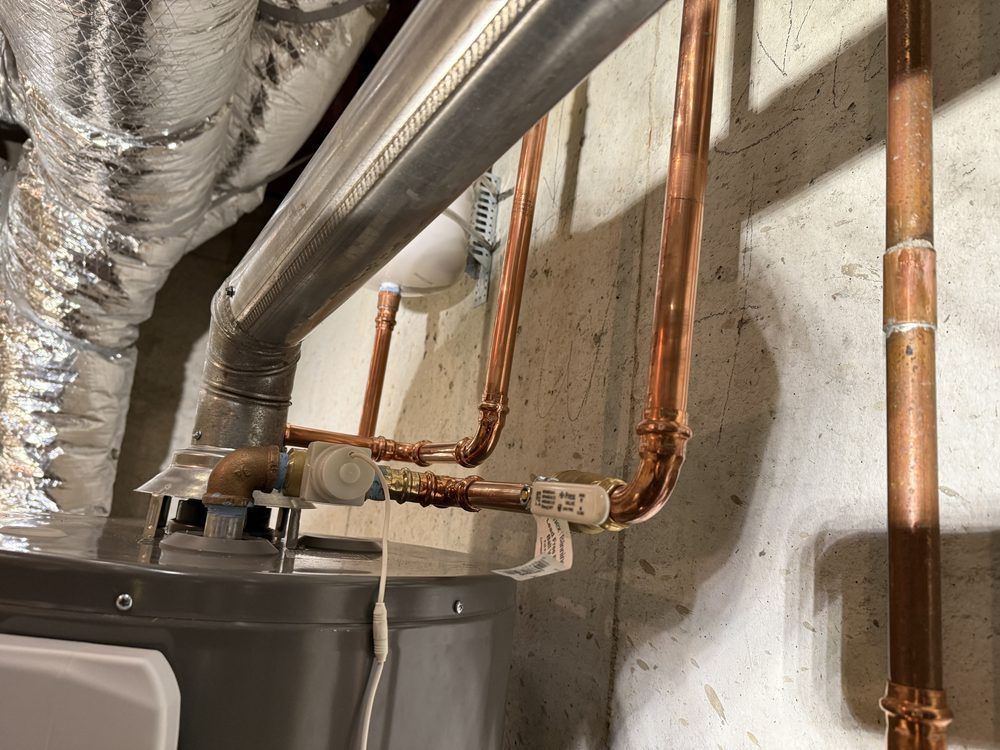 Copper pipes and insulated ducting above a water heater against a concrete wall