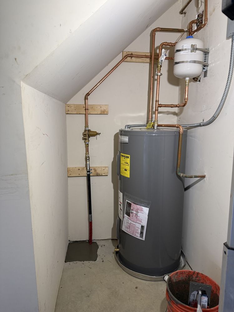Water heater and plumbing in a small utility closet under a sloped ceiling.