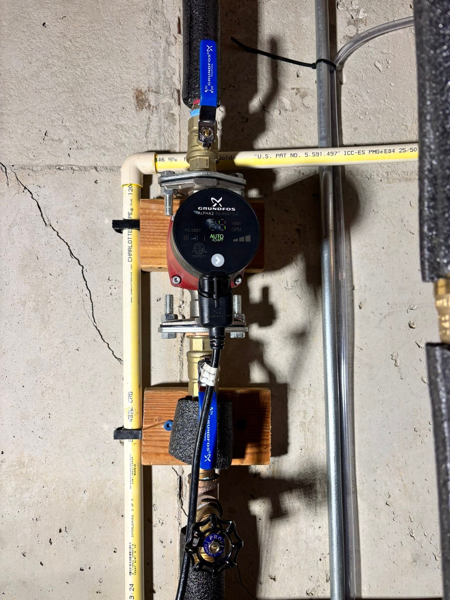 Wall-mounted plumbing manifold with yellow pipes, gauges, and blue shutoff valves against a concrete wall