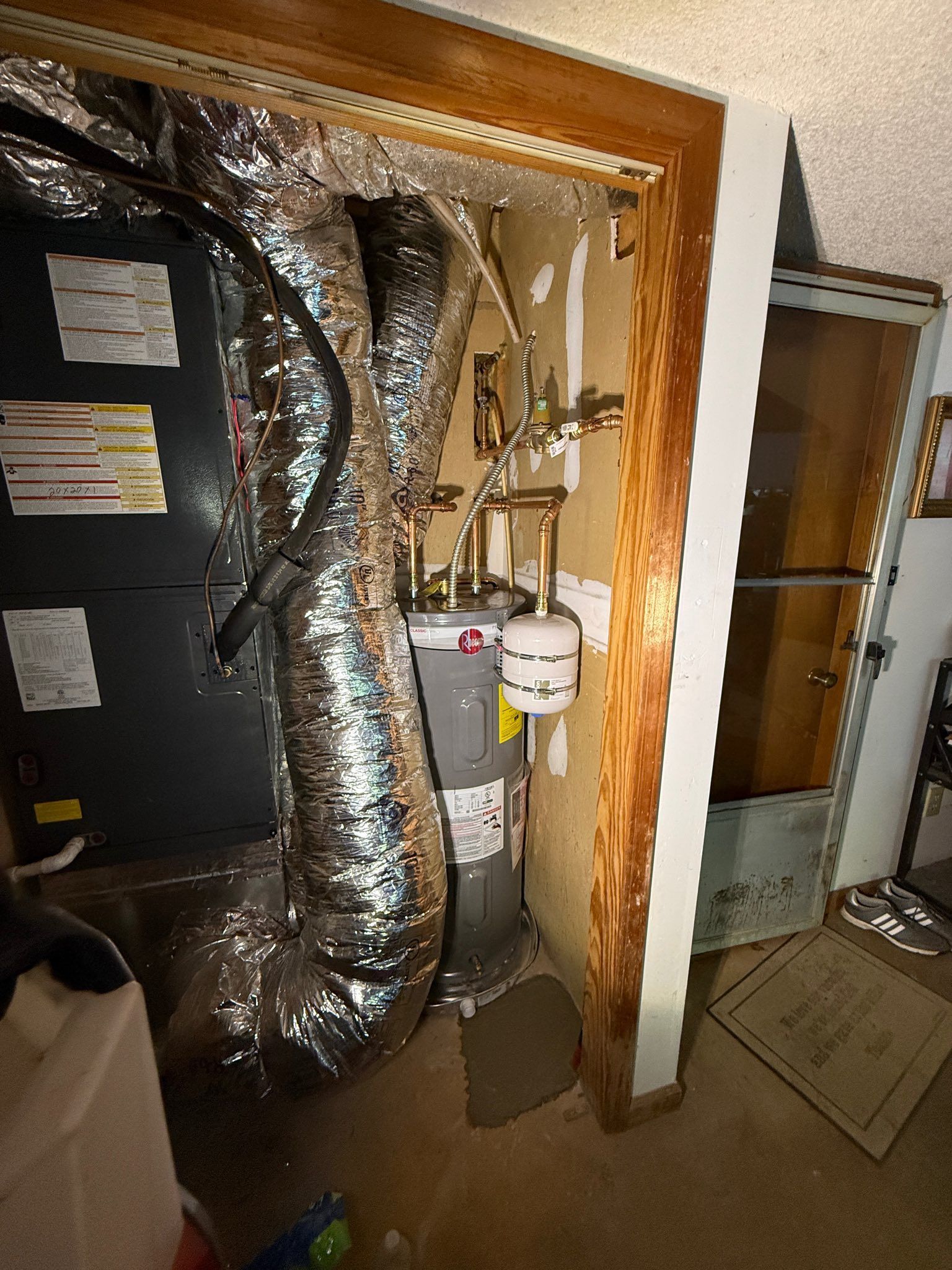 Open HVAC closet with silver ducting, furnace, pipes, and exposed framing in a utility area.