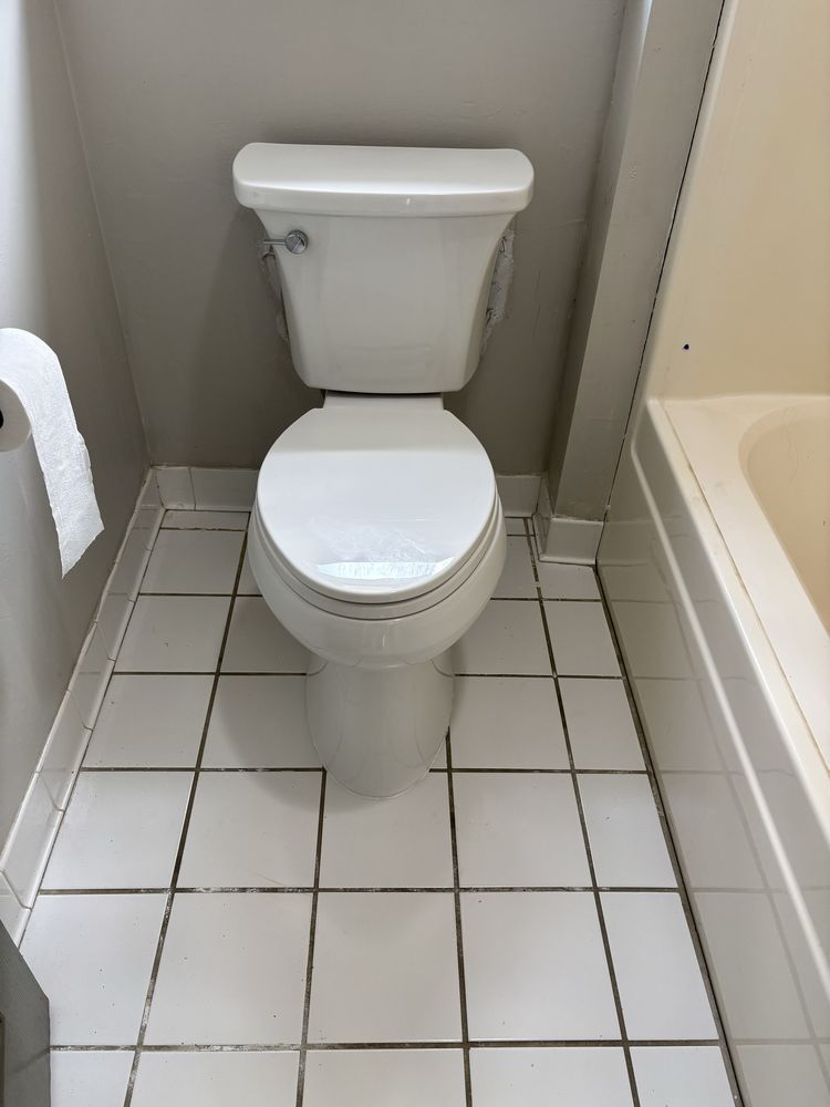 Small bathroom with a white toilet and bathtub, white tiled floor, and beige walls.