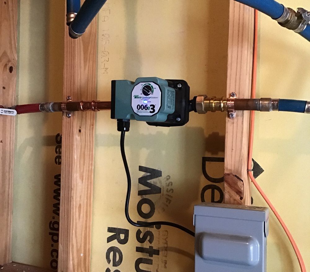 Water meter mounted on copper pipes inside an insulated wall cavity, with a digital display and white electrical box.