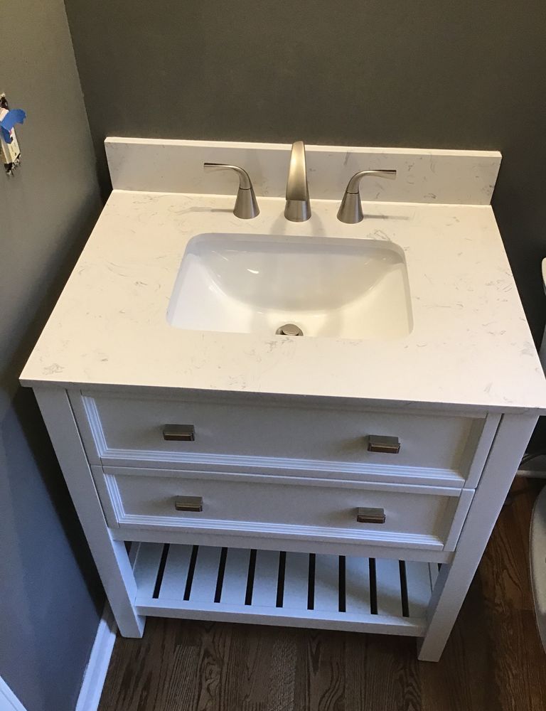 White bathroom vanity with sink, faucet, drawers, and slatted open shelf below.