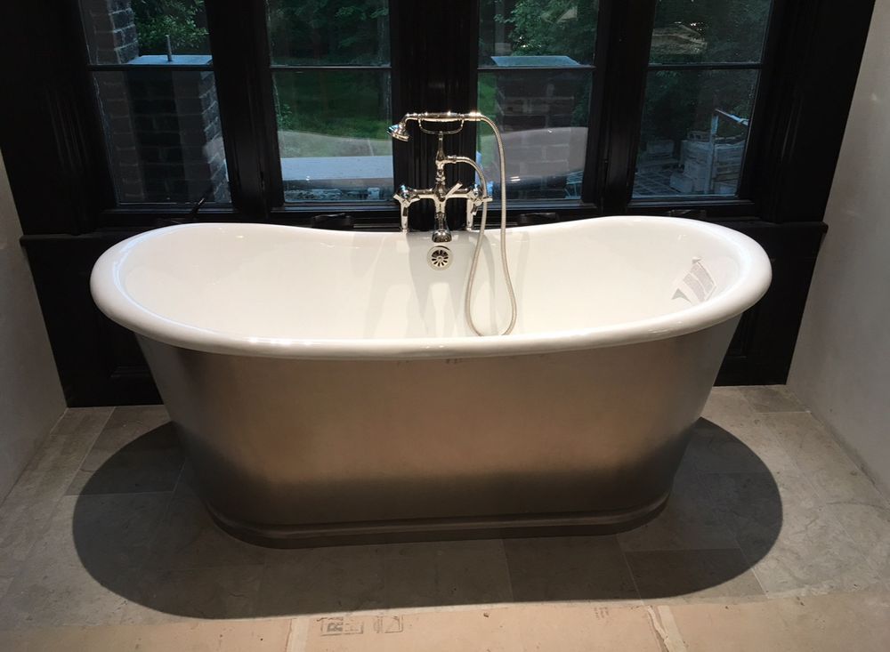 Modern white freestanding bathtub with chrome faucet in a tiled bathroom by a window