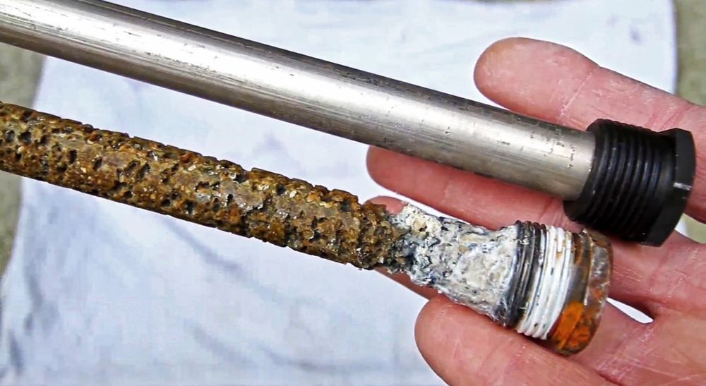 Rusty corroded metal rod held beside a shiny silver pipe with a black threaded cap