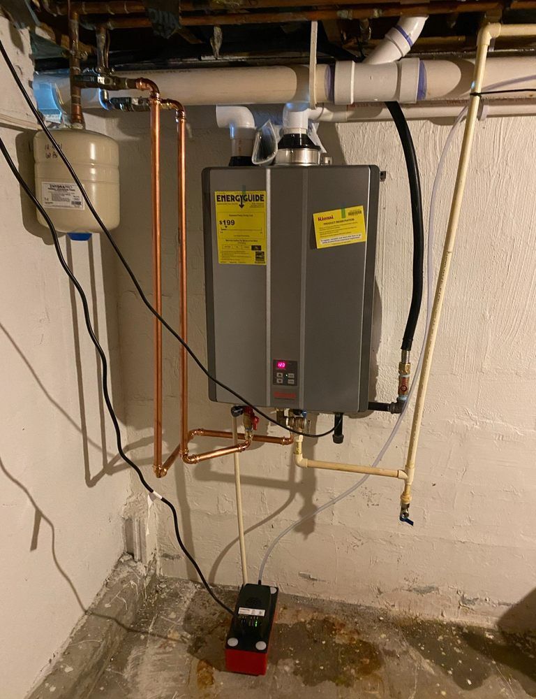 Basement water heater with copper pipes, a drain pan, and a red pump on a concrete floor.