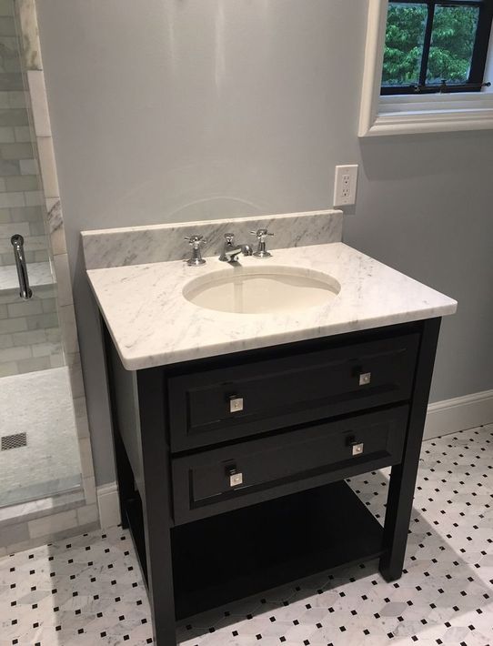 Black bathroom vanity with white countertop and sink beside a shower.