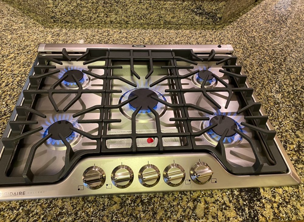 Stainless steel gas cooktop on a granite countertop with five burners and control knobs.