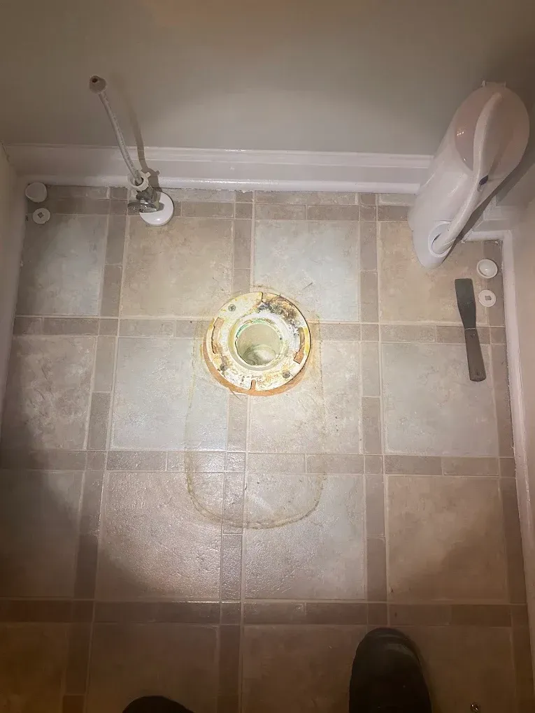 Shower floor with a central drain, beige tile, and a white showerhead and fixture visible.