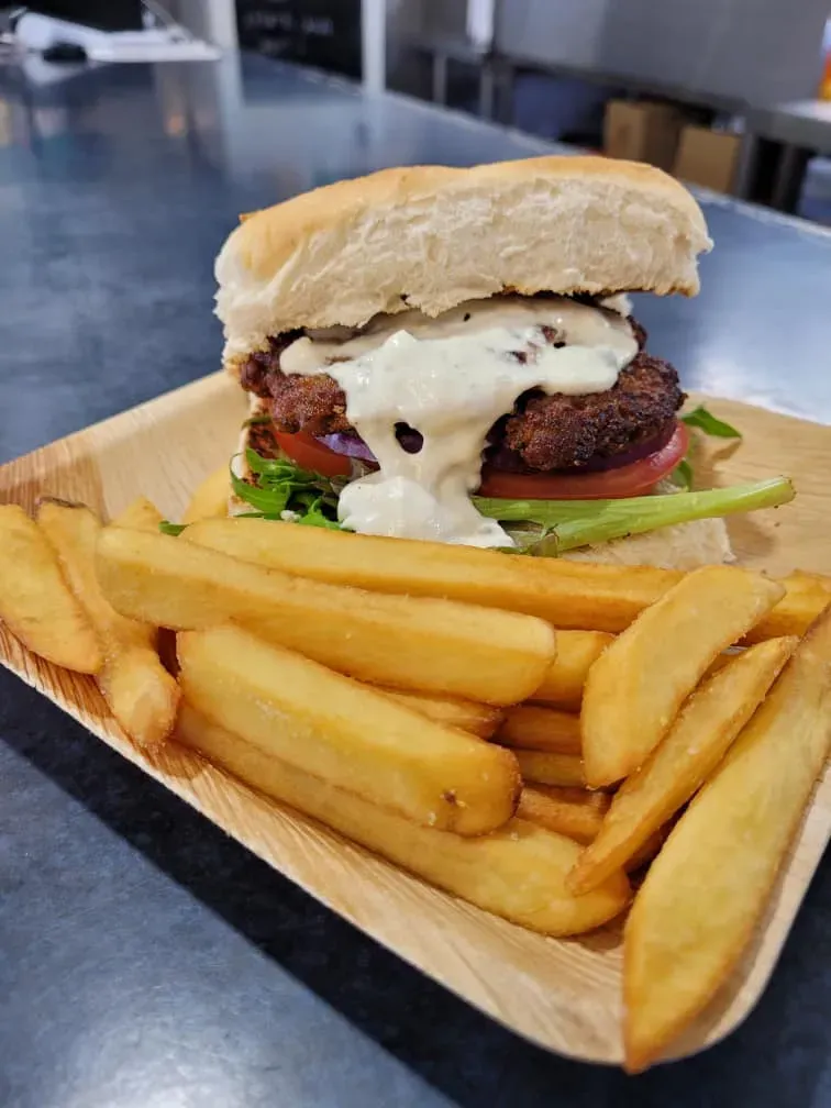 A Hamburger and French Fries on a Wooden Plate on a Table — Stones Oysters & Shed Takeaway in Harrington, NSW