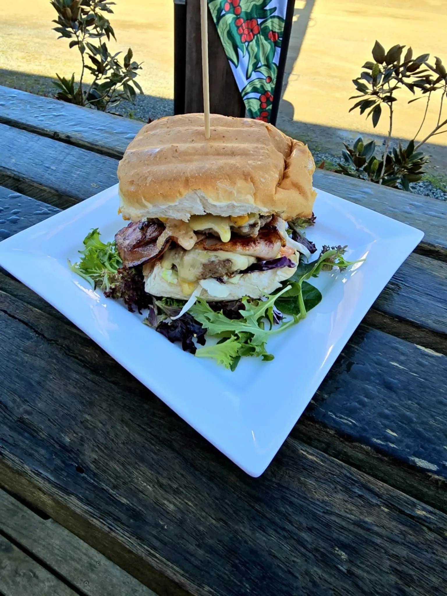 A Hamburger is Sitting on a White Plate on a Wooden Table — Stones Oysters & Shed Takeaway in Taree, NSW