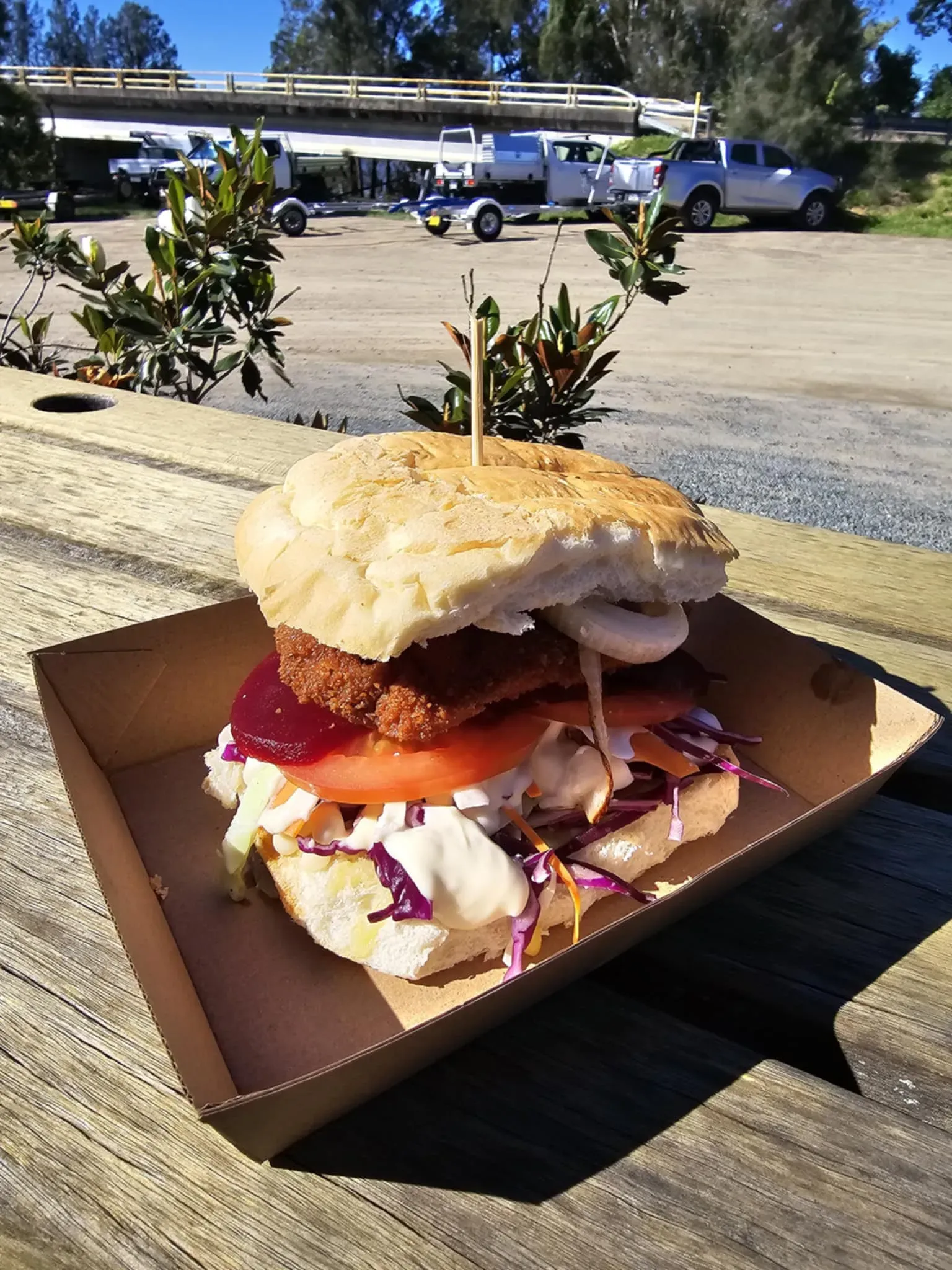 A Sandwich is Sitting on a Cardboard Tray on a Wooden Table — Stones Oysters & Shed Takeaway in Harrington, NSW