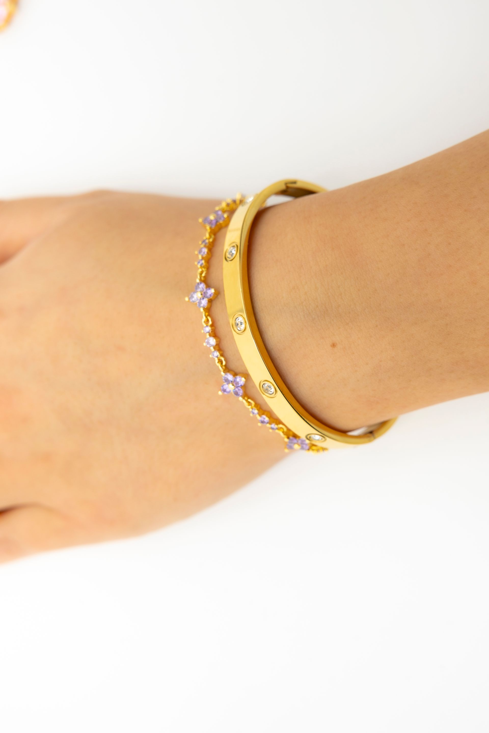 Nahaufnahme eines Handgelenks, an dem ein goldener Armreif mit Schraubenmotiv und ein zierliches goldenes Kettenarmband.