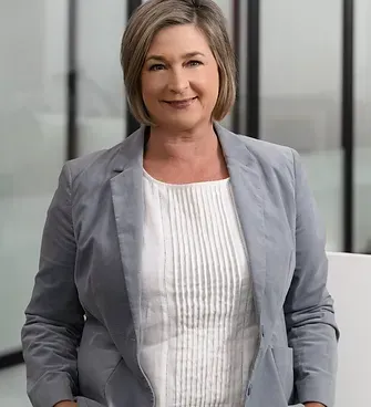 A woman in a grey jacket and white shirt is smiling for the camera.
