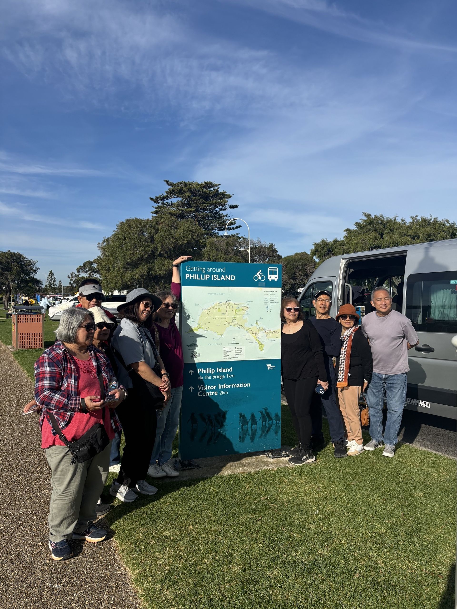 A group of friends standing beside a tourist sign with the Ticket 2 Ride minibus in the background.