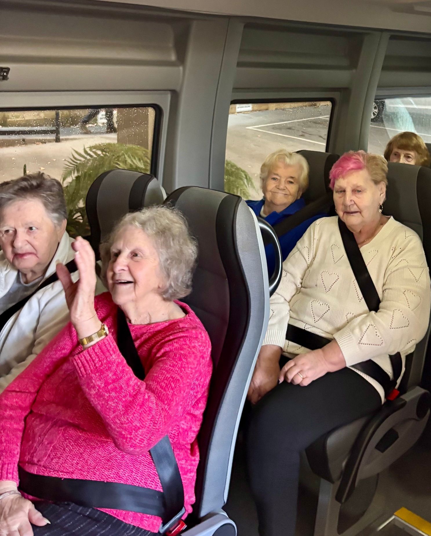 A group of seniors in a Ticket 2 Ride minibus, some smiling, waving while enjoying a day trip.
