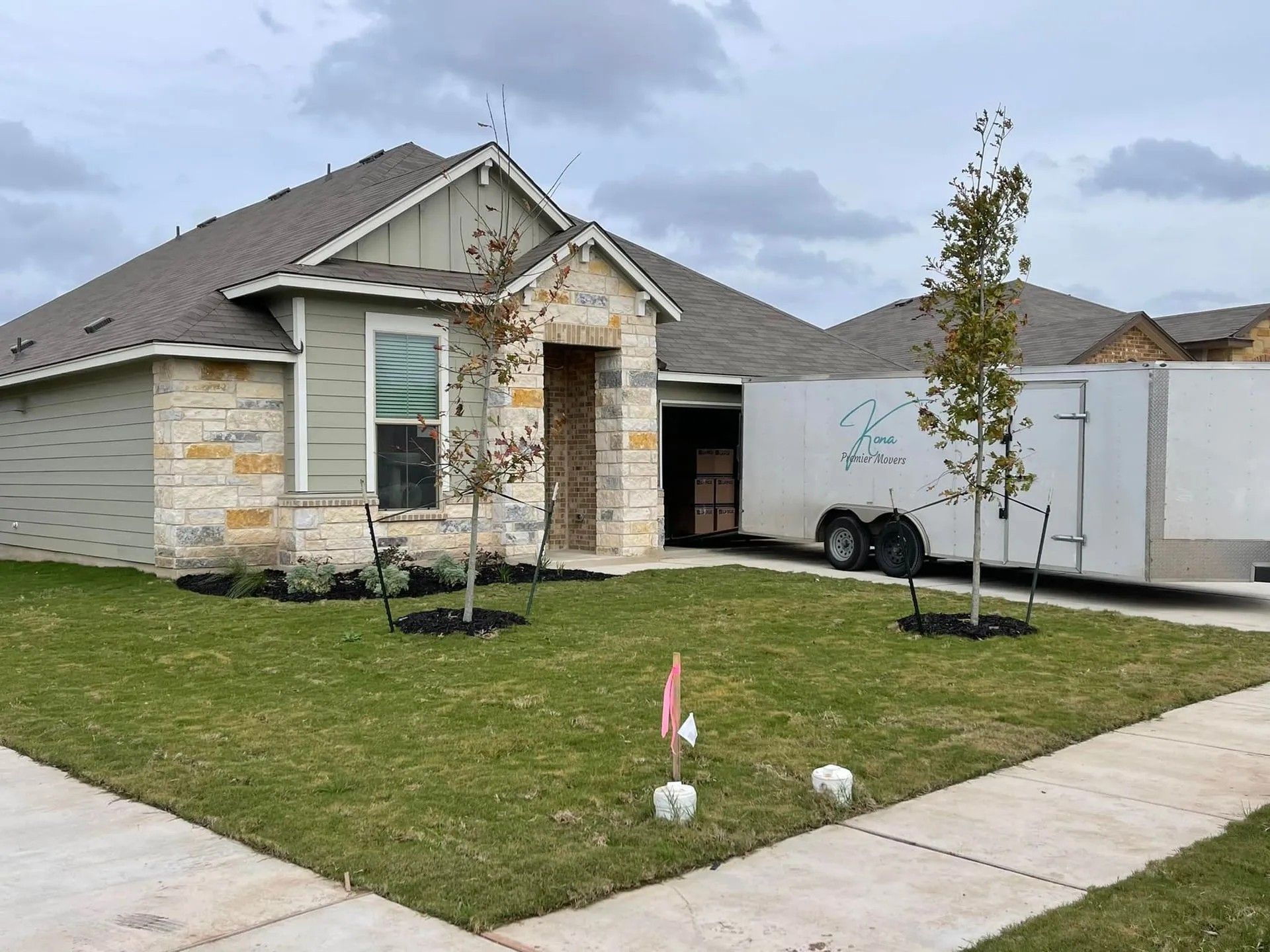 Single-story house with stone facade, front lawn, young trees, and a white moving truck in the driveway.