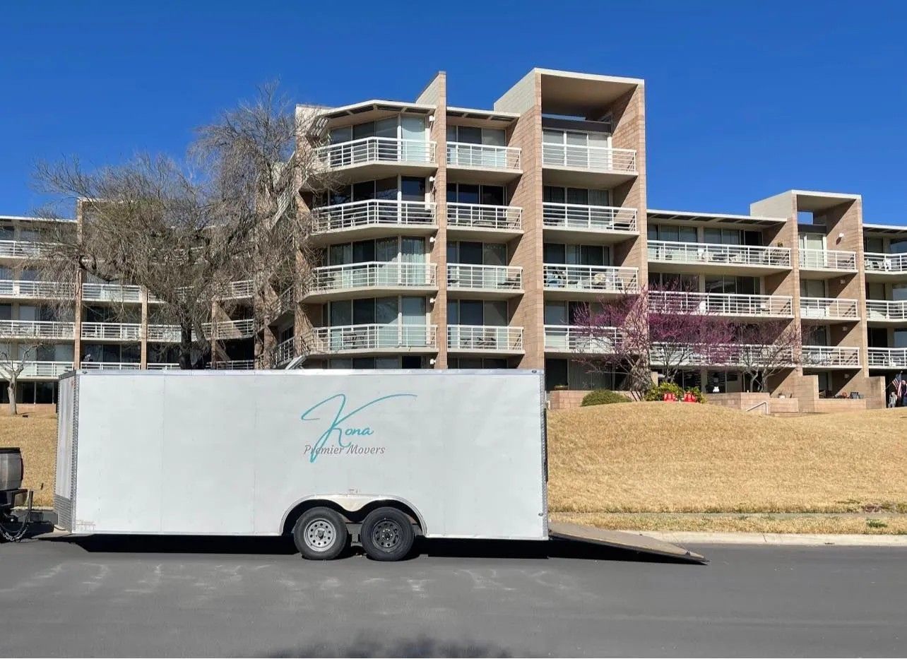 White enclosed trailer parked on a street in front of apartment buildings and bare trees.