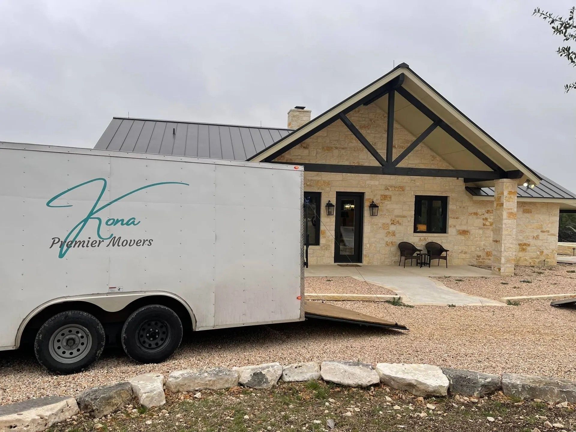 White trailer parked beside a beige stone house with black trim and a gravel driveway