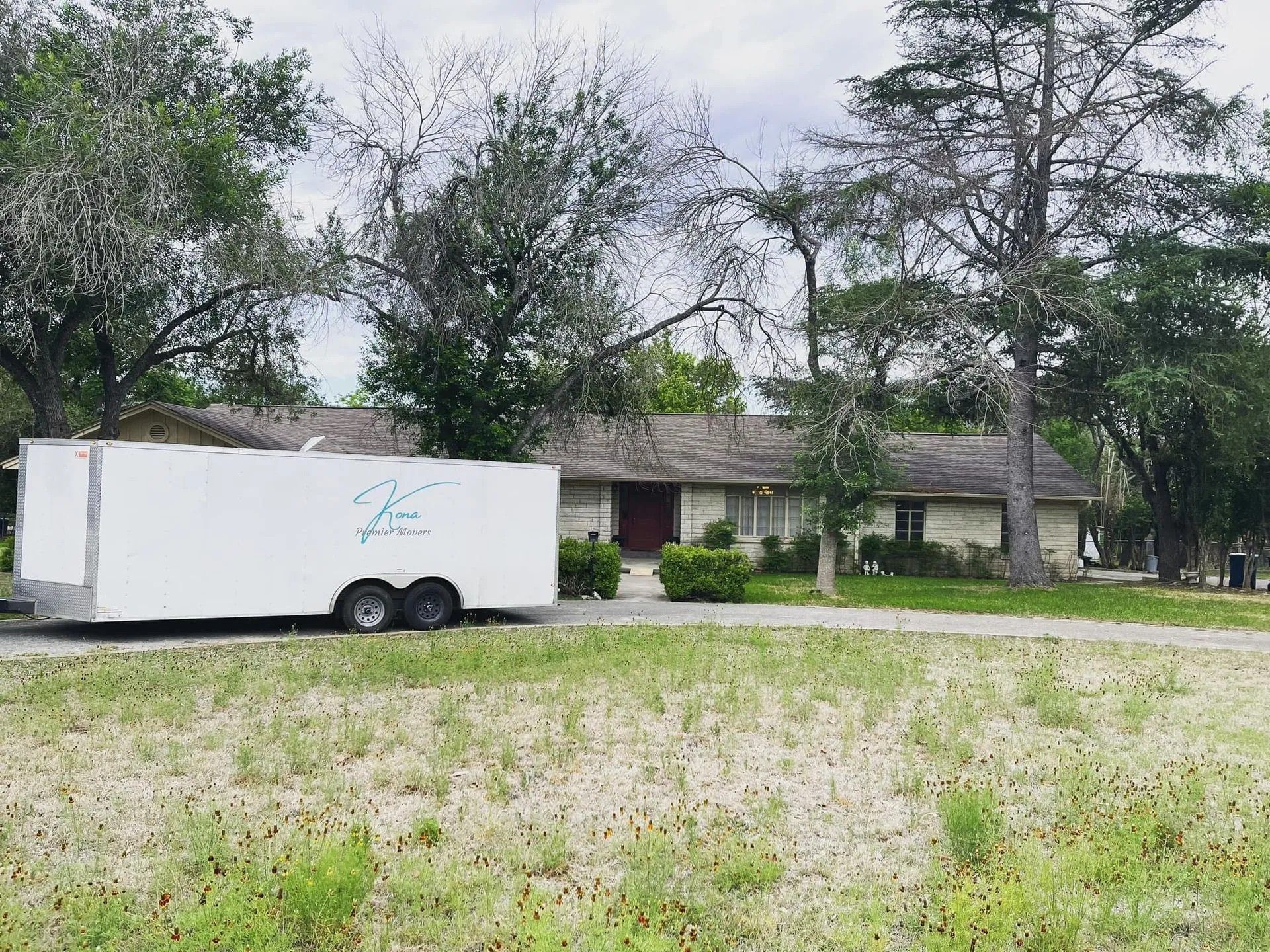 White trailer parked on a grassy lot in front of a low building and trees.