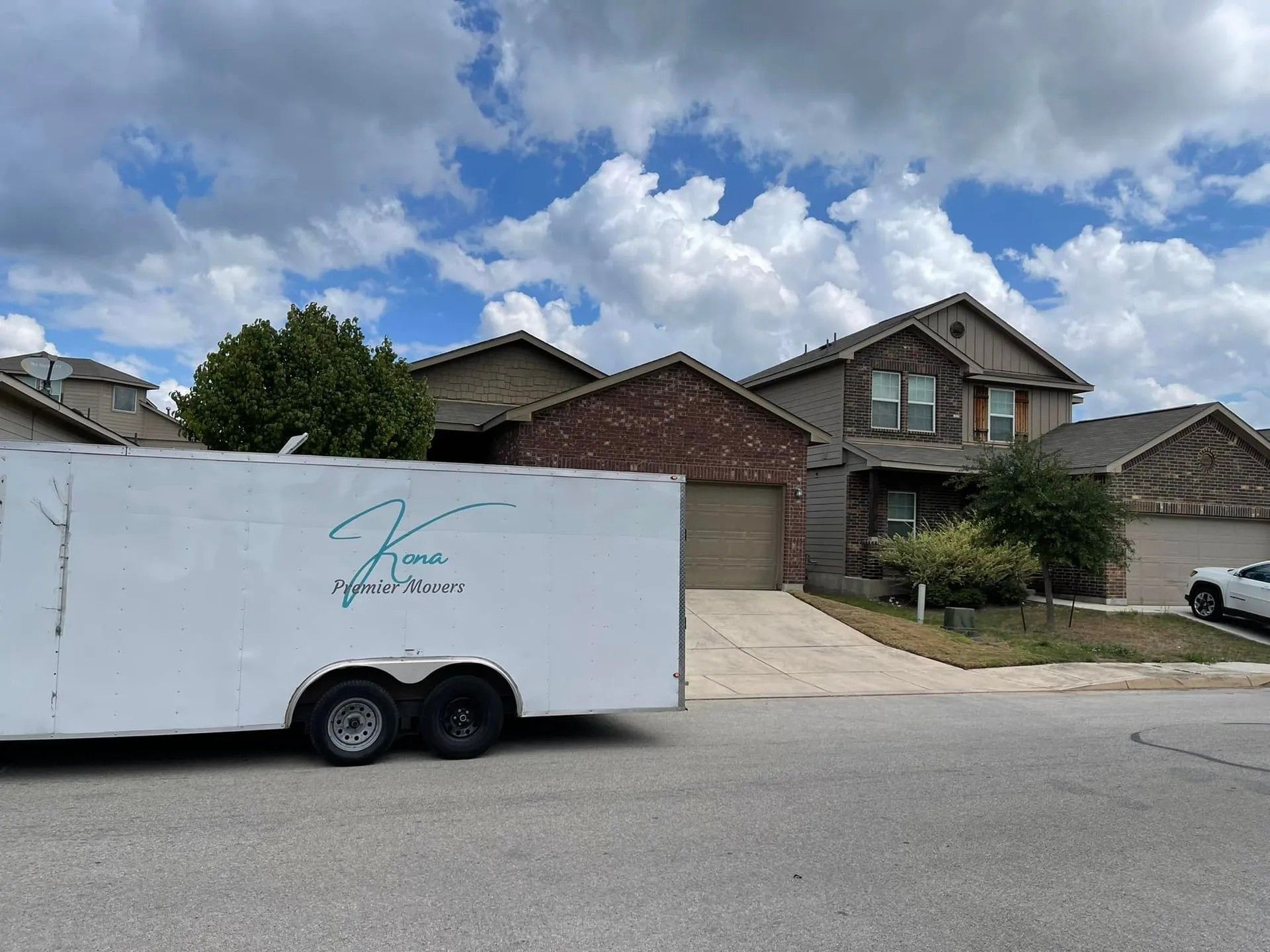 White trailer parked on a suburban street in front of brick houses under a cloudy sky.