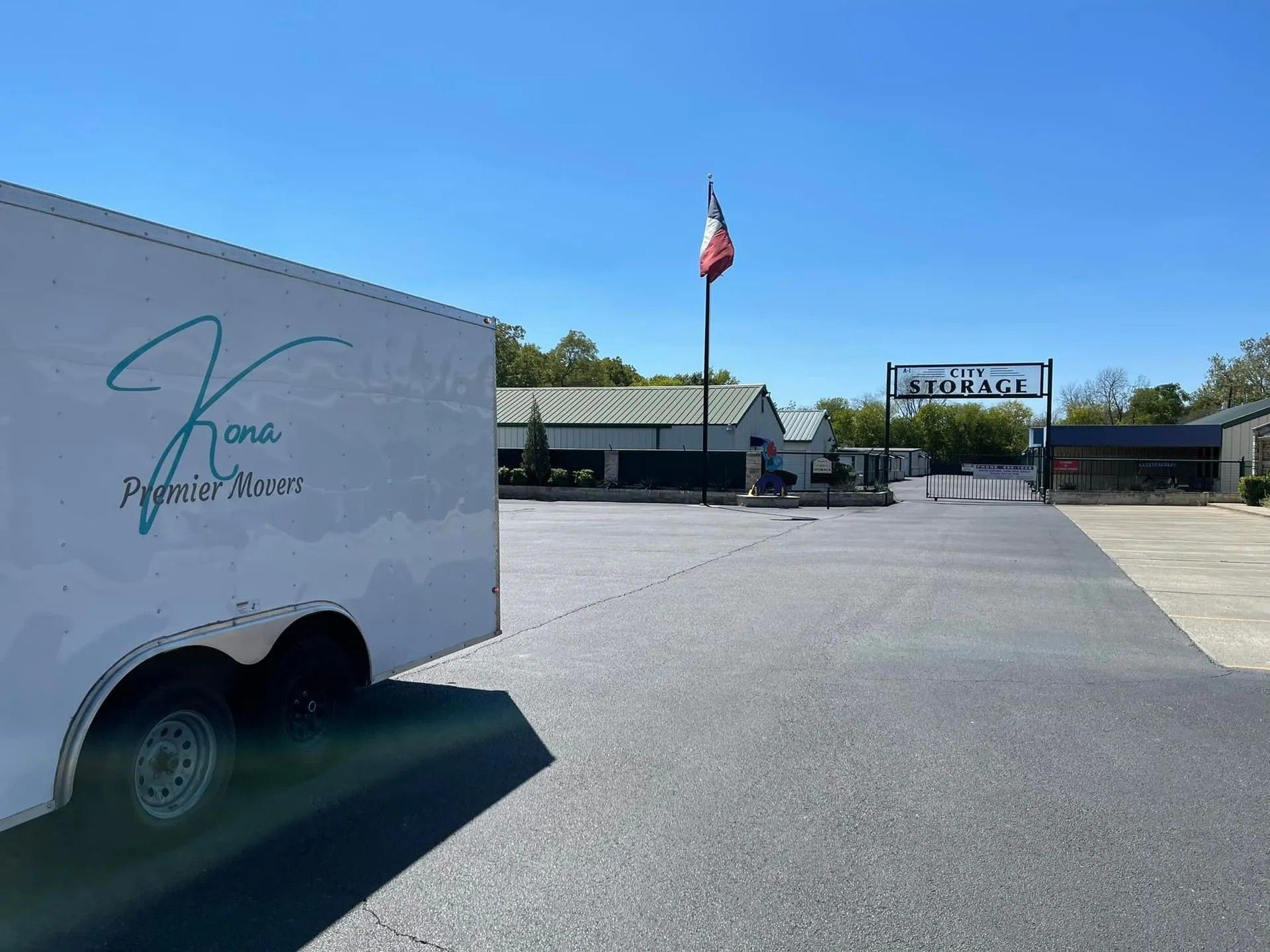 White truck at a sunny parking lot entrance with an American flag and a gated sign in the background