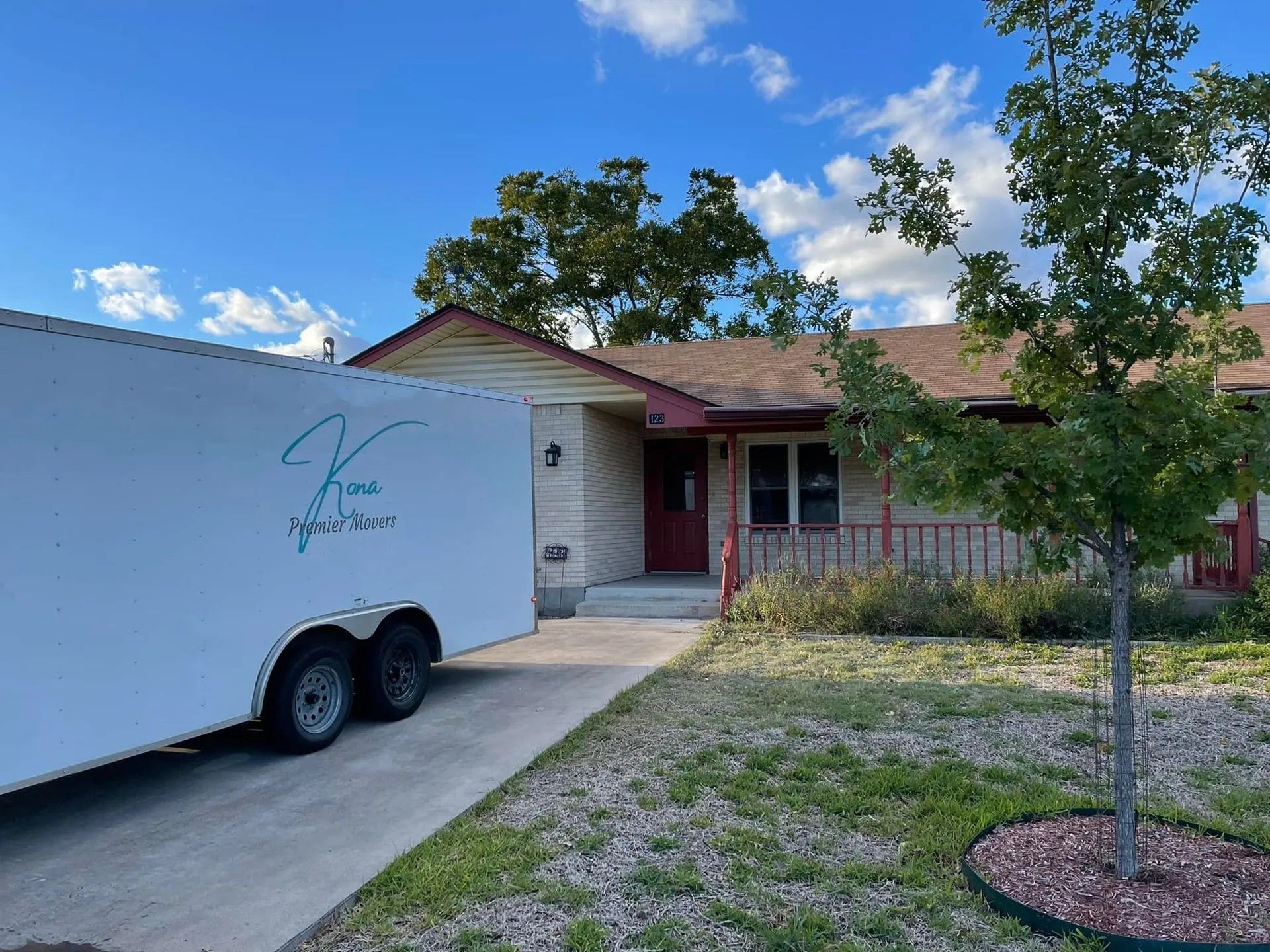 Single-story house with a white trailer parked in the driveway and a small front yard tree.