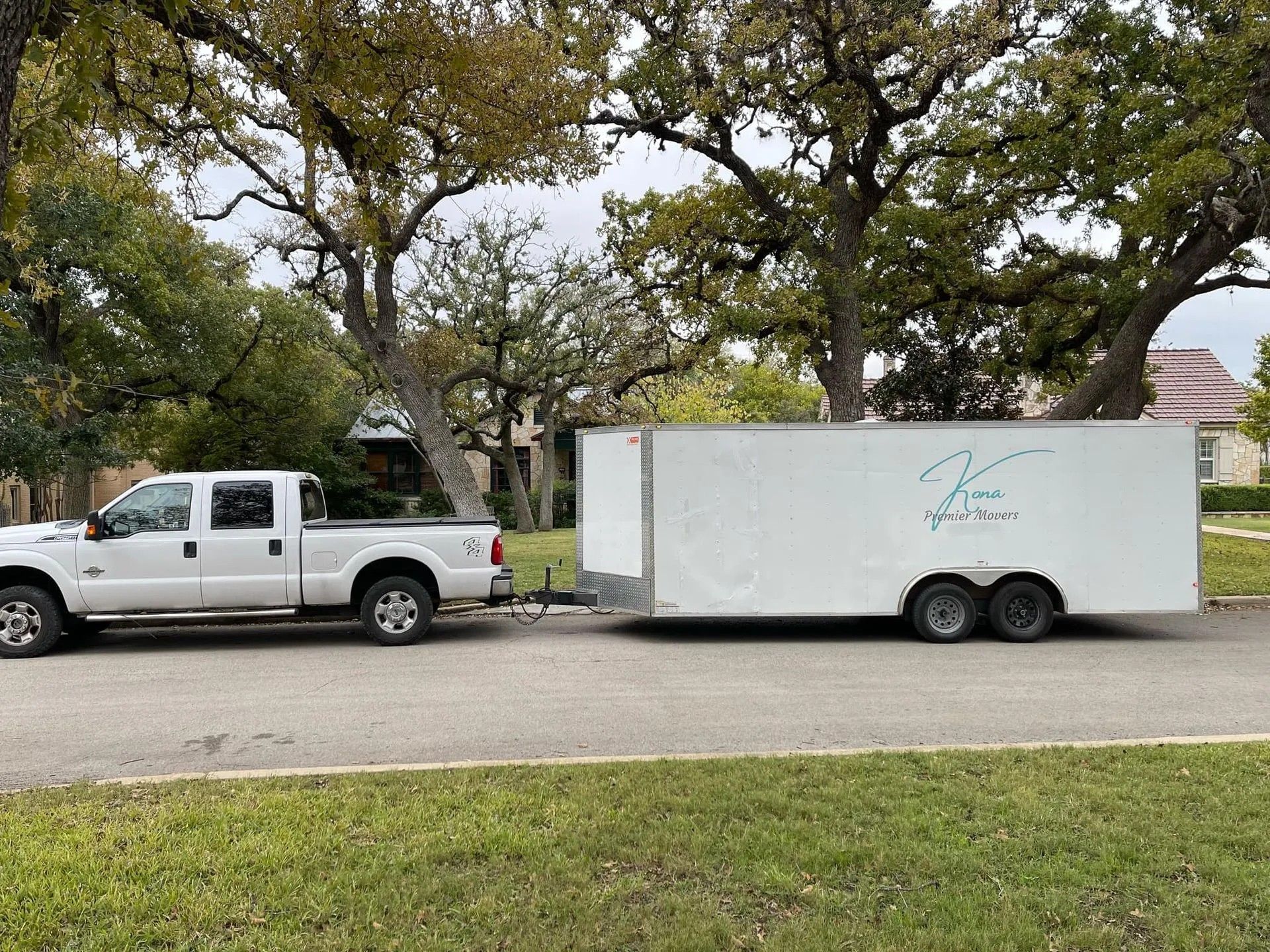 White pickup truck towing a white enclosed trailer parked along a tree-lined street