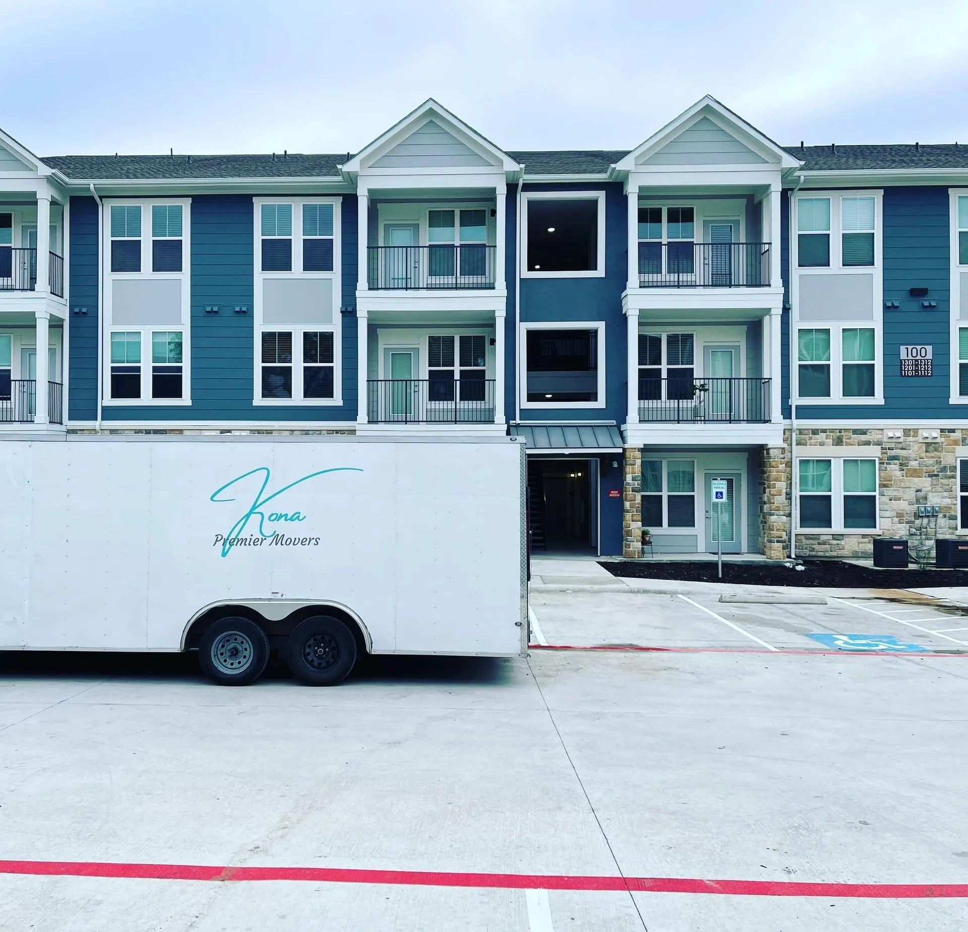 White box truck parked in front of teal-and-gray apartment buildings with a red-striped pavement in foreground
