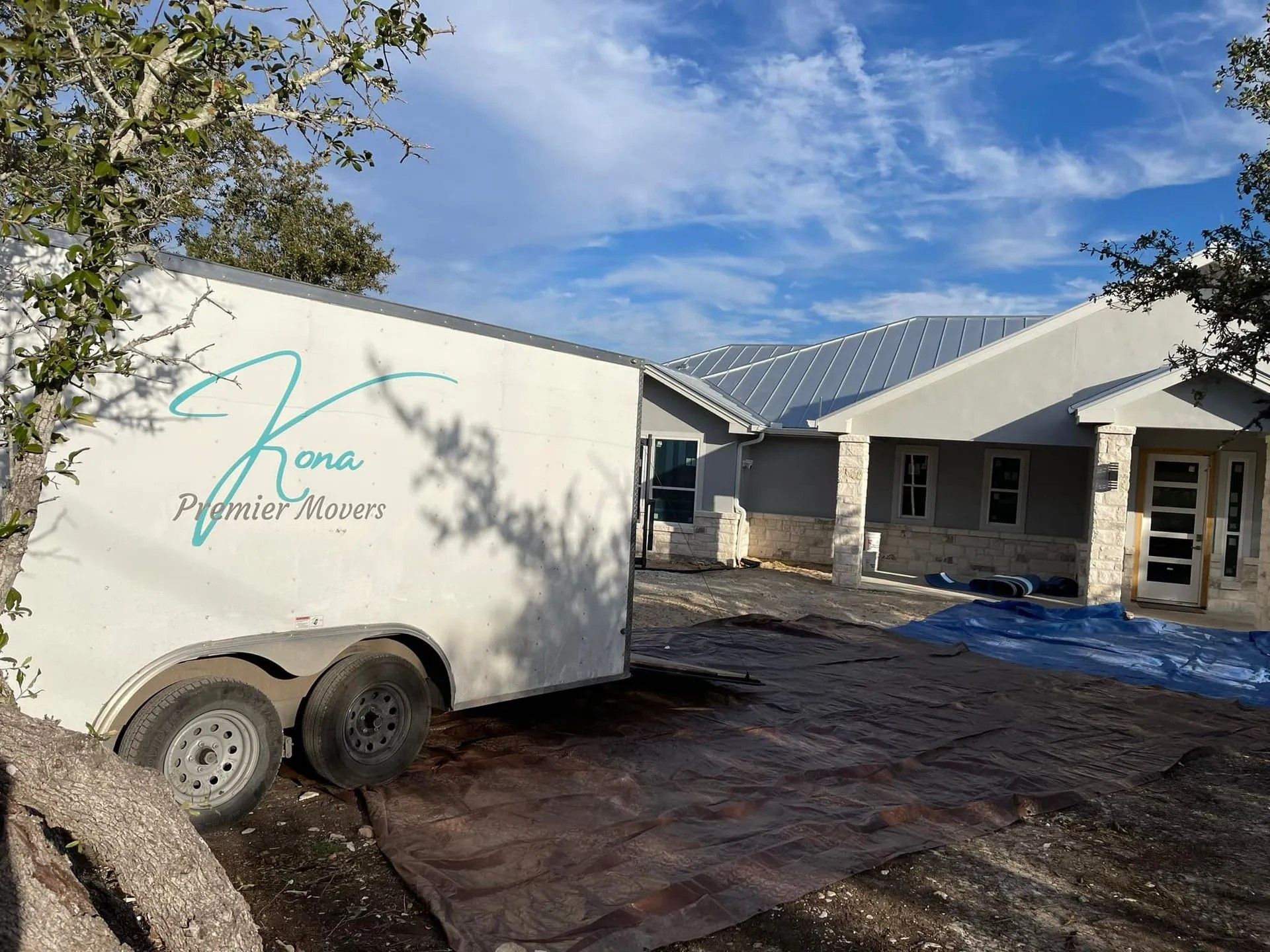 White trailer beside a partially built house with solar panels and muddy construction ground under a blue sky