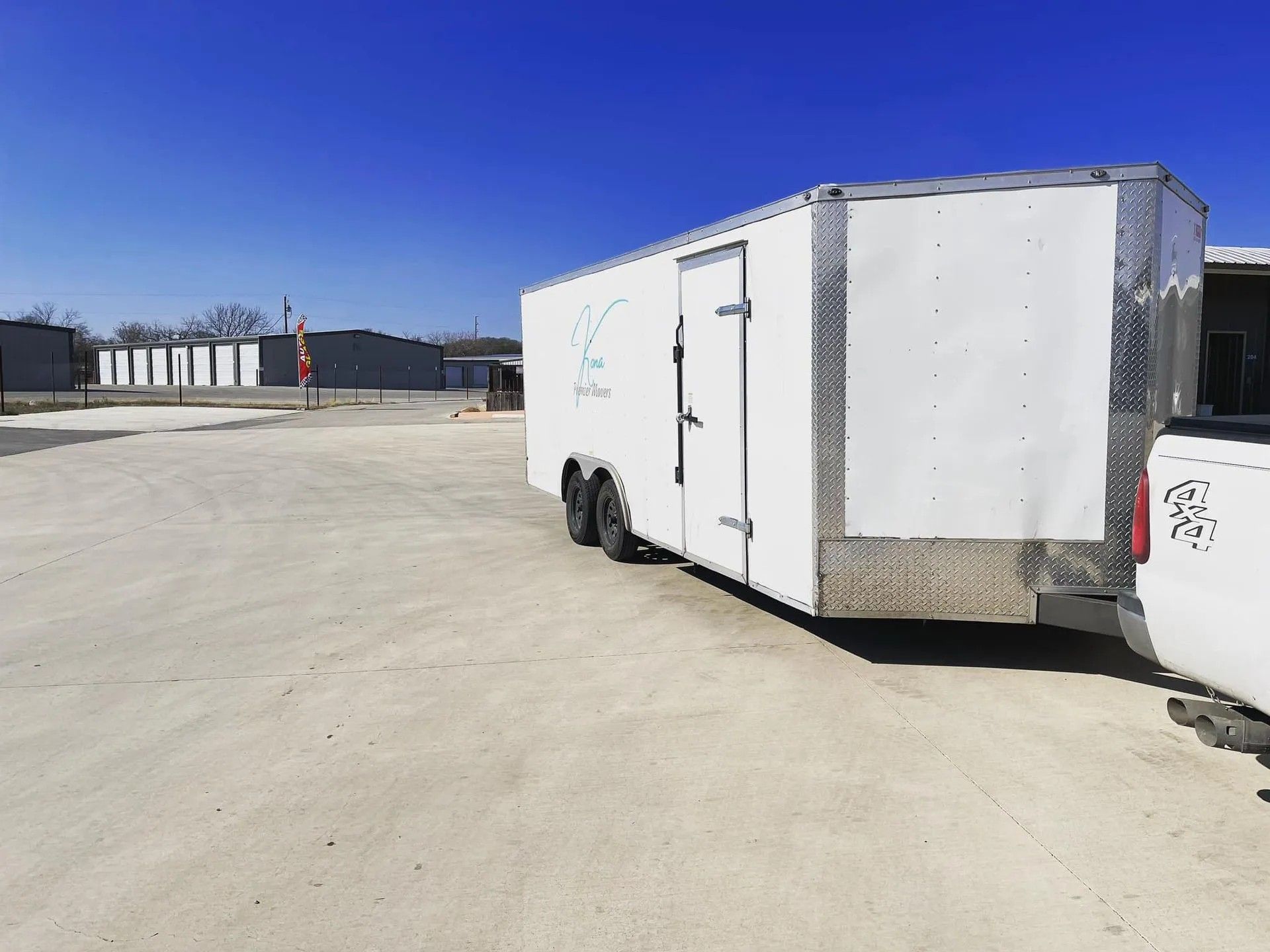 White enclosed trailer parked on a sunlit concrete lot under a clear blue sky.