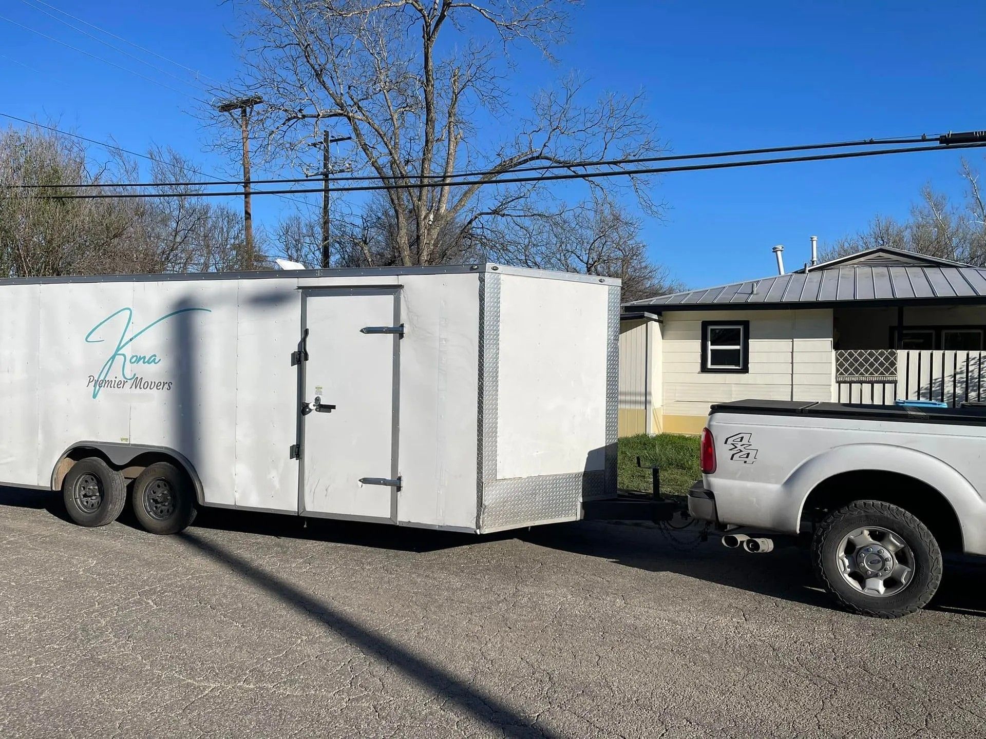 White enclosed trailer hitched to a silver pickup truck parked on a gravel driveway near a house