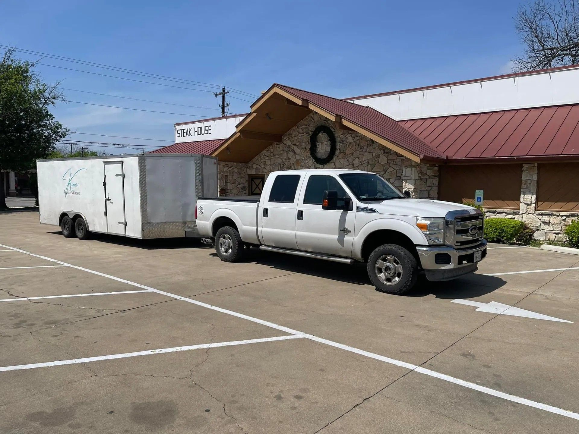 White pickup truck towing a white trailer parked in front of a brick building on a sunny day