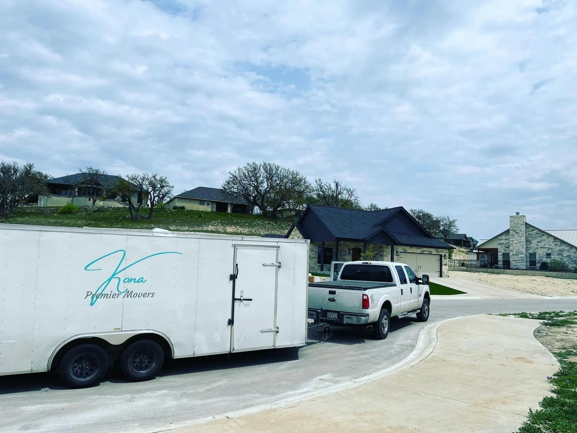 White pickup towing a white trailer on a curved suburban driveway under a cloudy sky