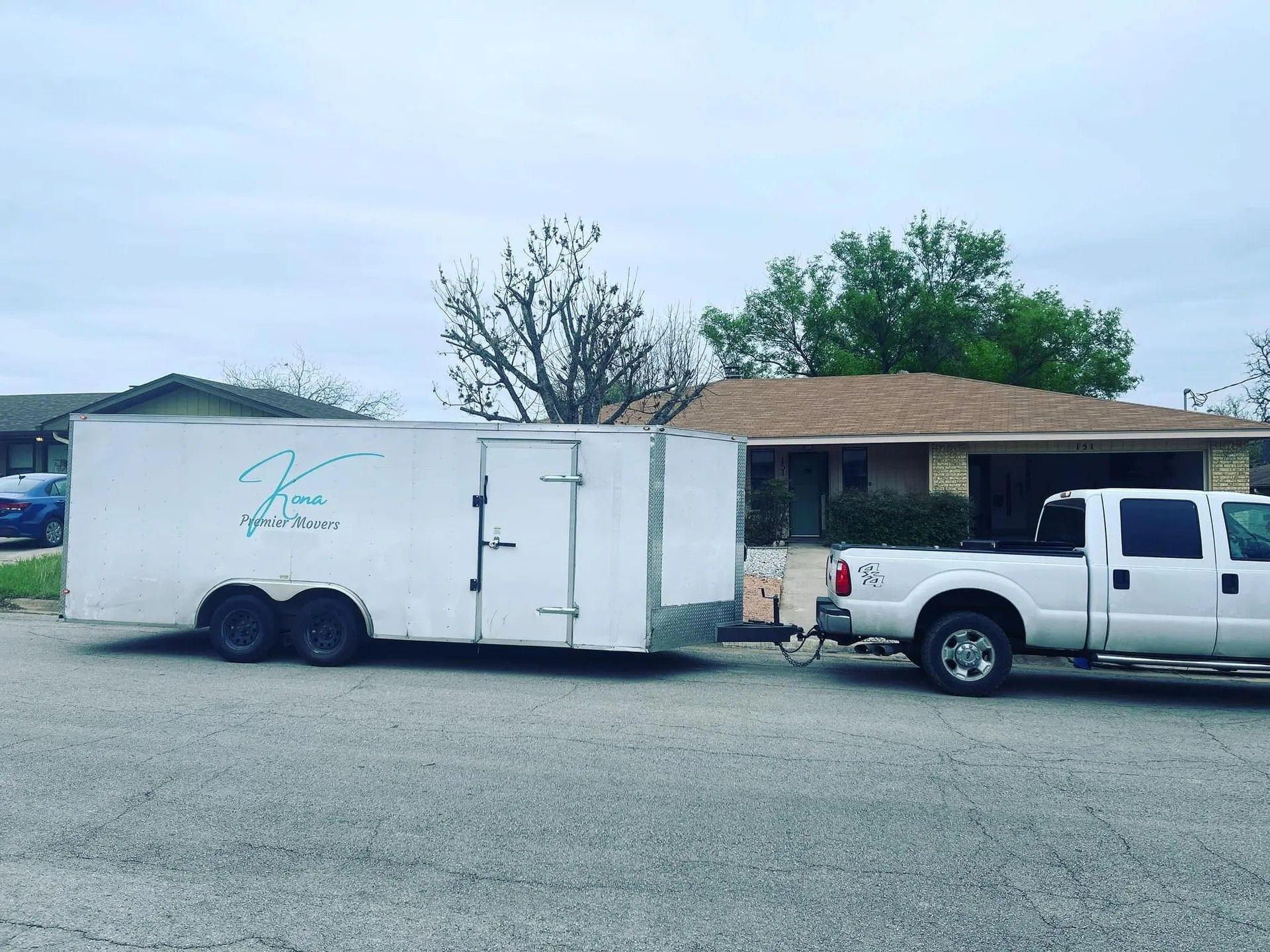 White pickup truck towing a white enclosed trailer parked beside a small building under a cloudy sky