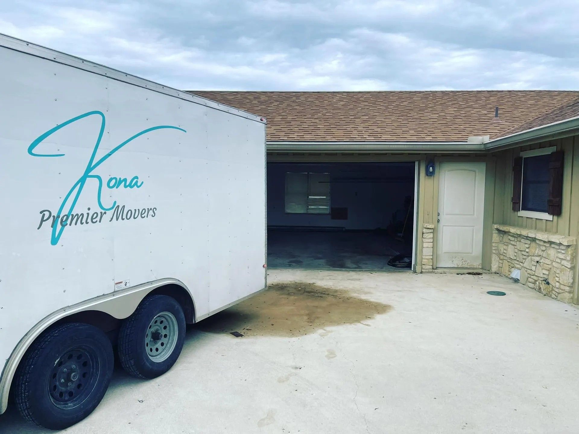 White trailer with “Kona Premier Homes” parked beside a house with an open garage.