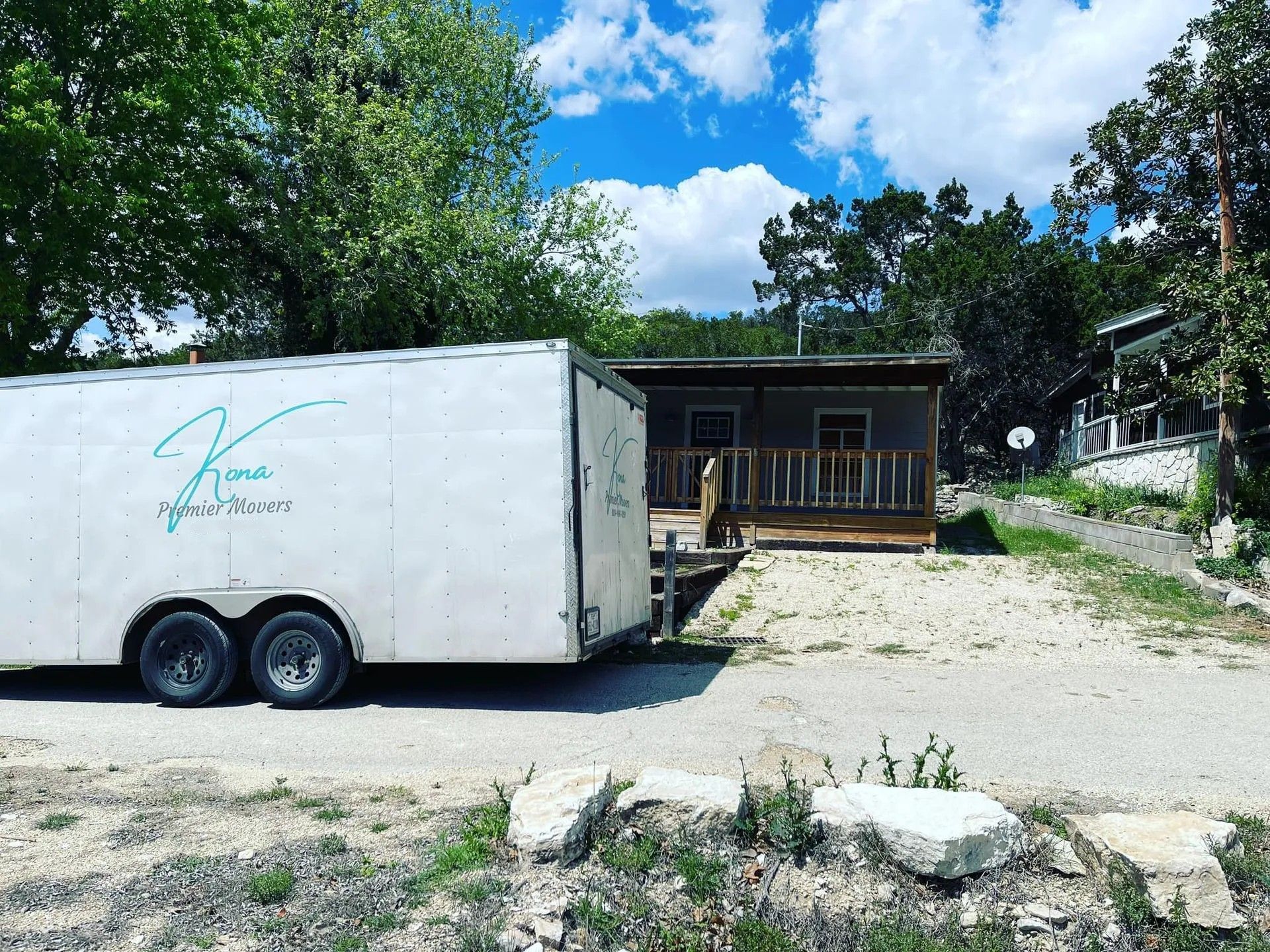 White enclosed trailer parked by a small house on a sunny day, with trees and blue sky in the background