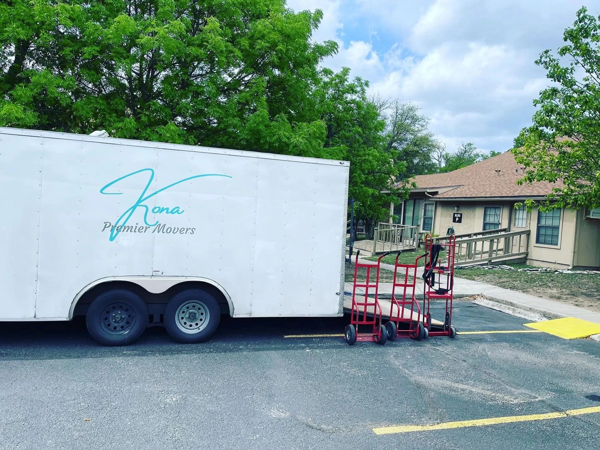 White trailer with logo and red lift equipment parked outside a house on a residential street.