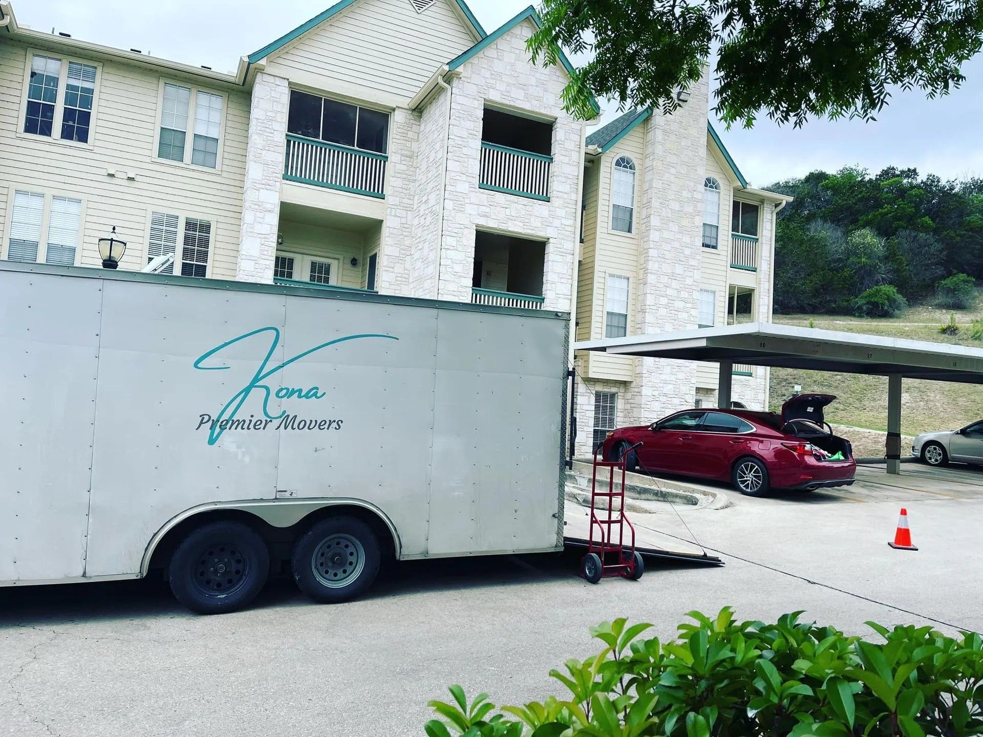 Red truck parked beside a white trailer in front of an apartment building, with a carport and cones nearby