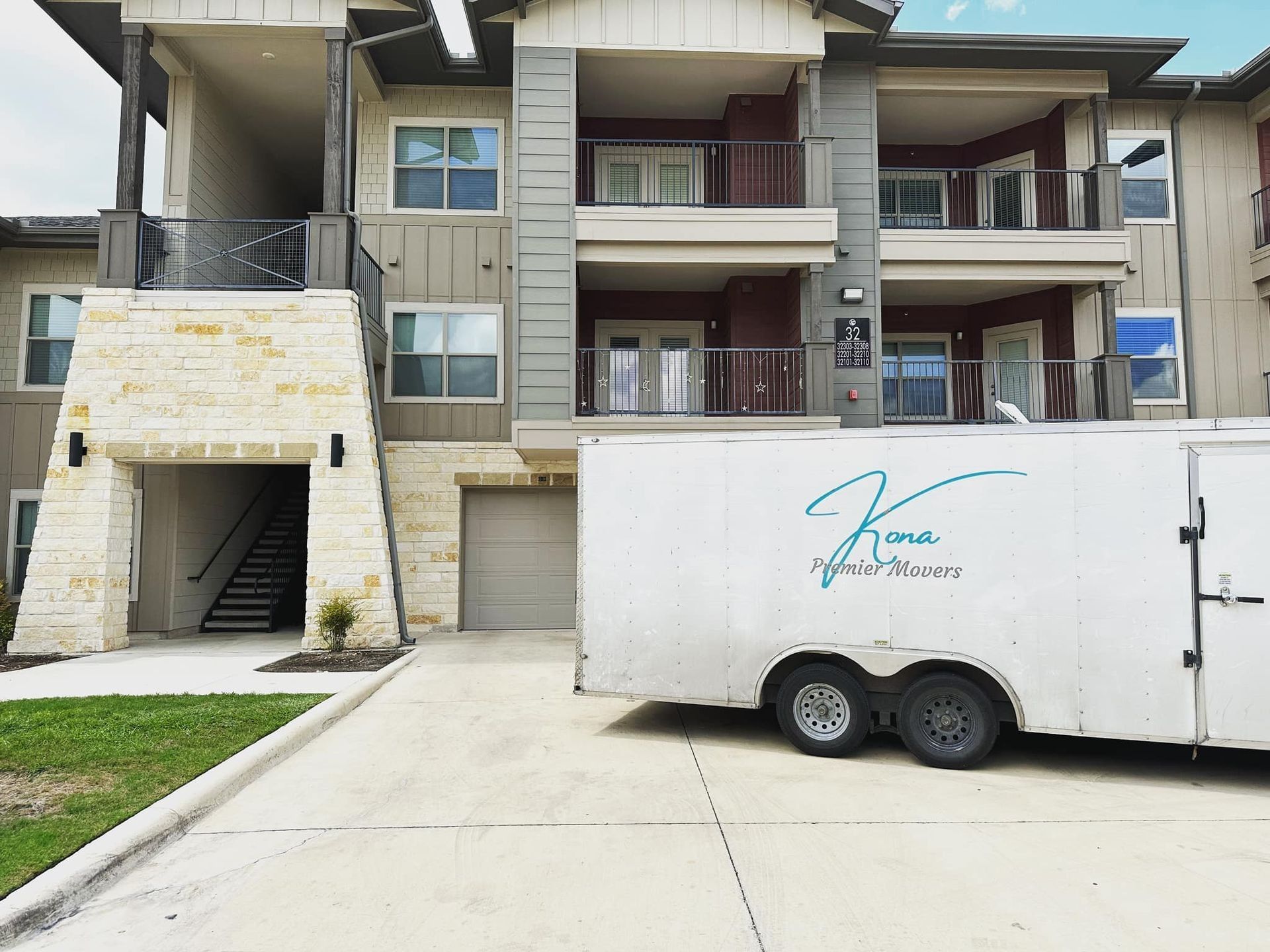 Apartment building with balconies and a white trailer parked in front of a concrete driveway
