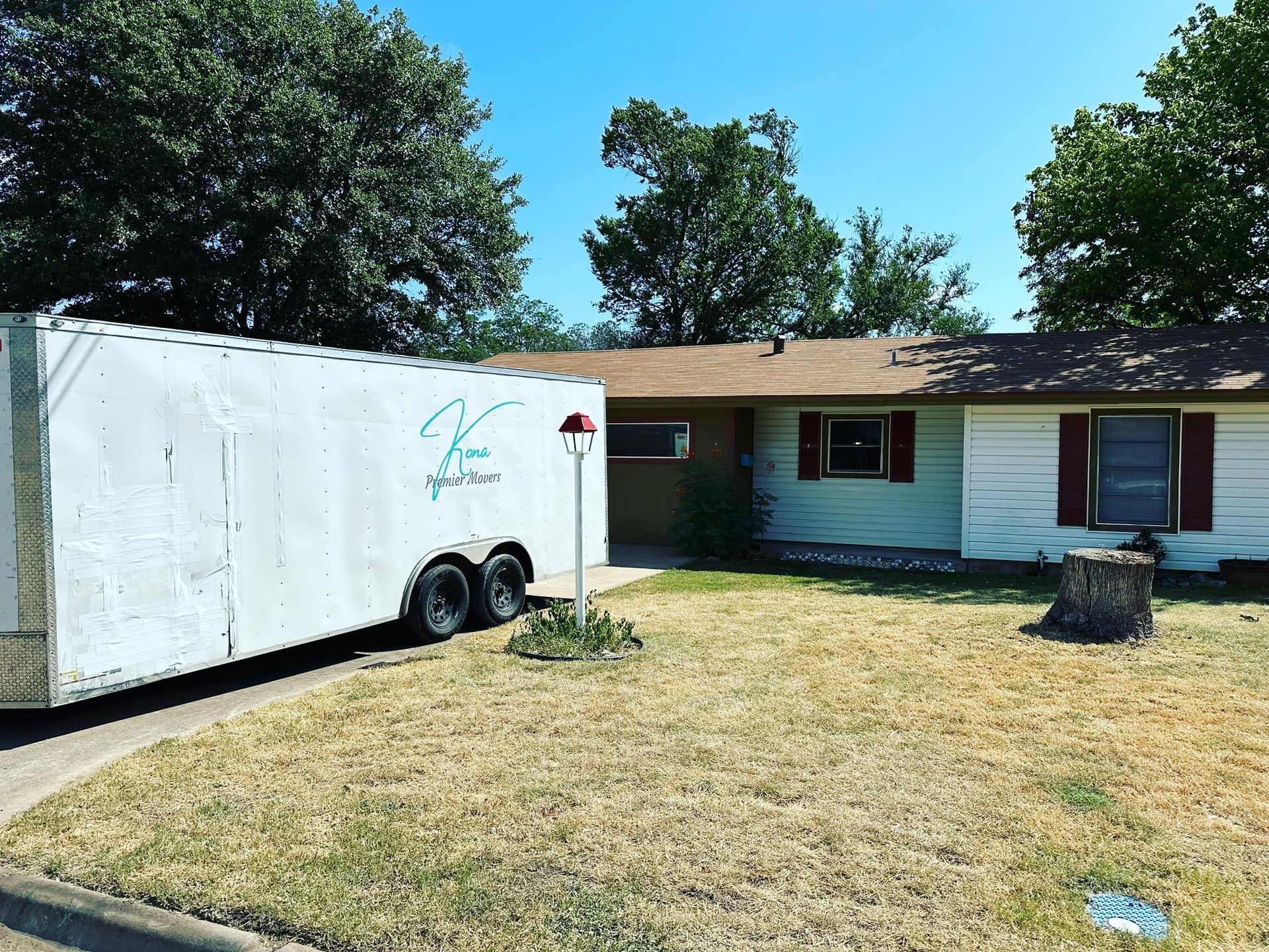 White enclosed trailer beside a single-story house with a dry front yard and trees behind it