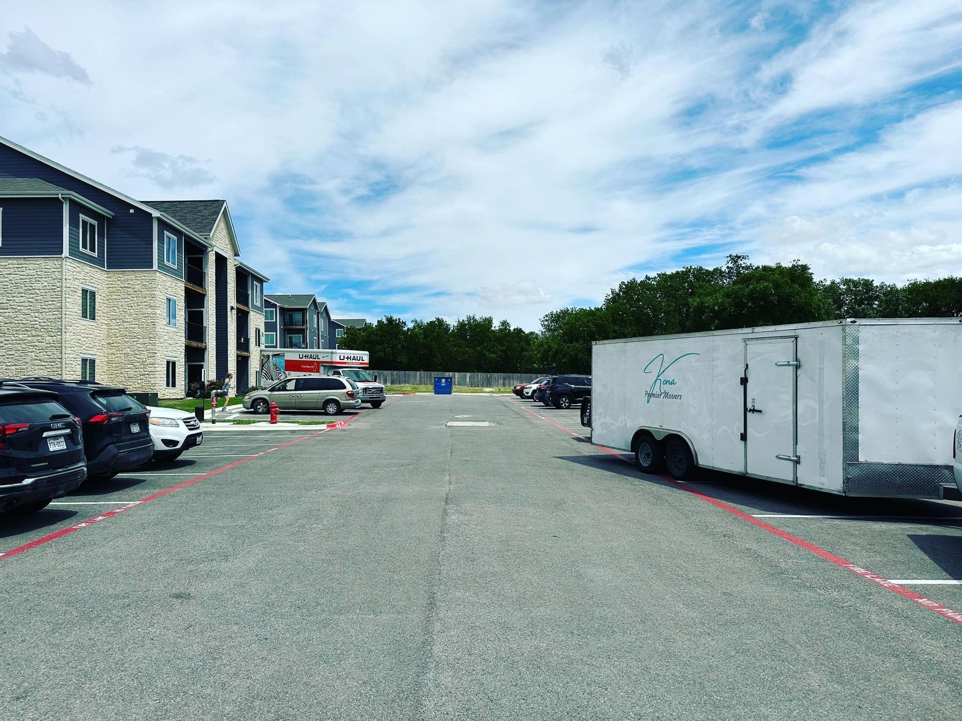 Apartment parking lot with cars, a white trailer, and blue sky above stone buildings
