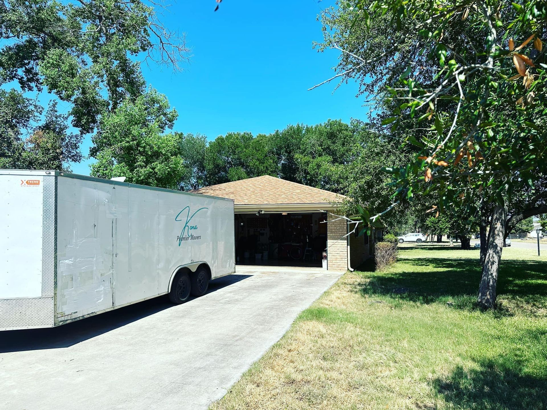 White moving truck parked in a driveway beside a house and garage on a sunny day.