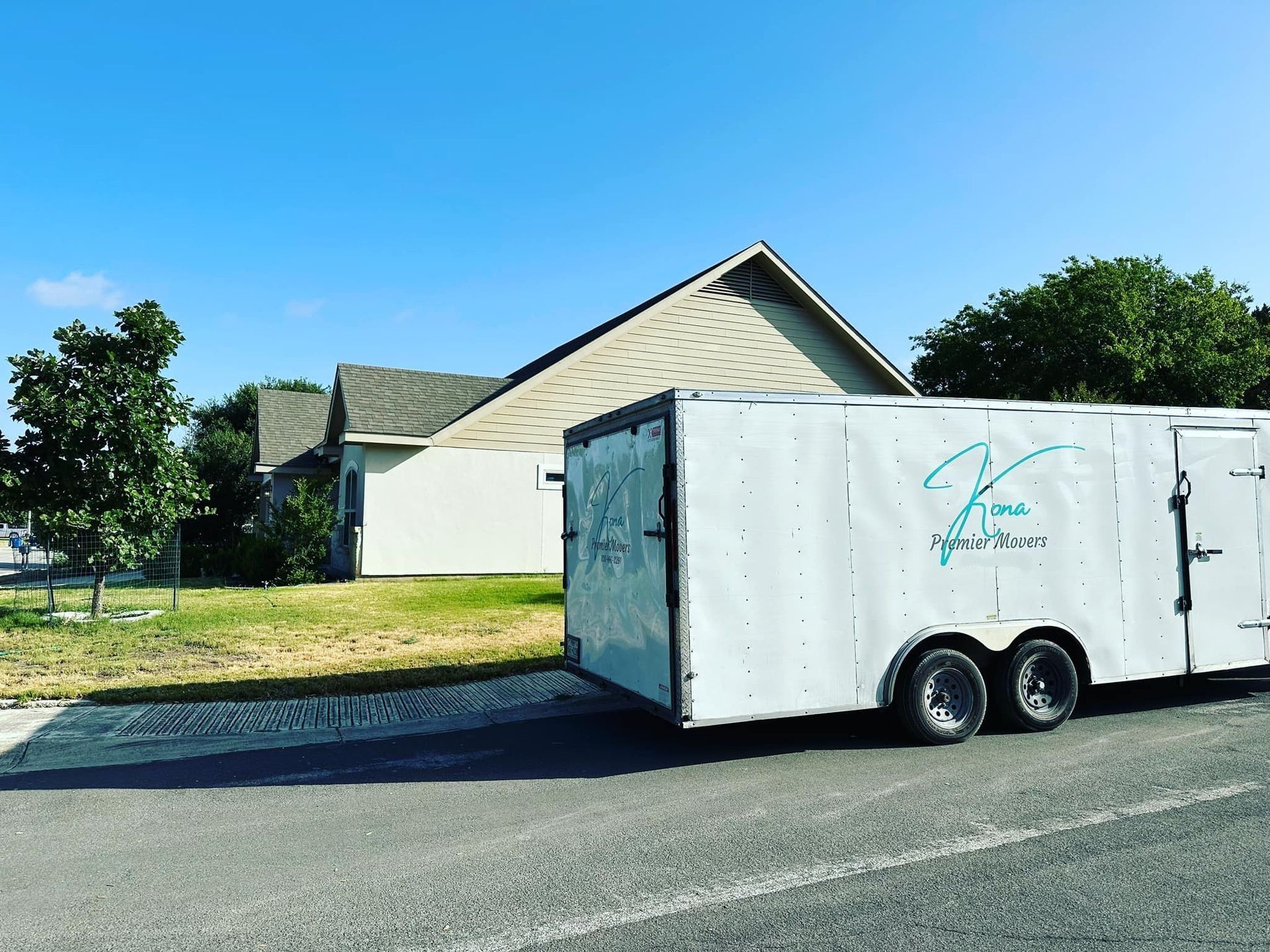 White enclosed trailer parked on a street in front of a house on a sunny day