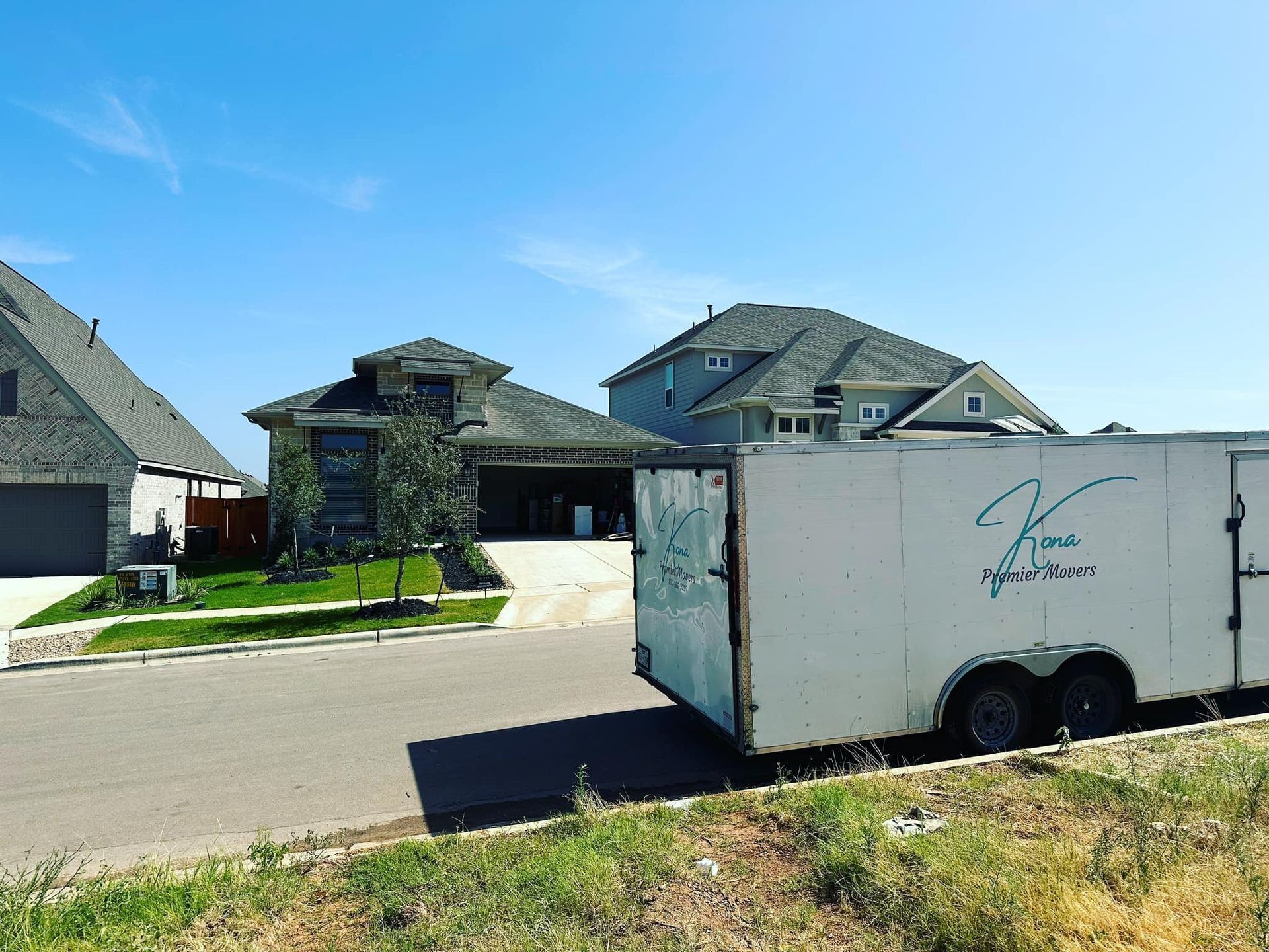 White utility trailer on a residential street in front of modern houses under a clear blue sky