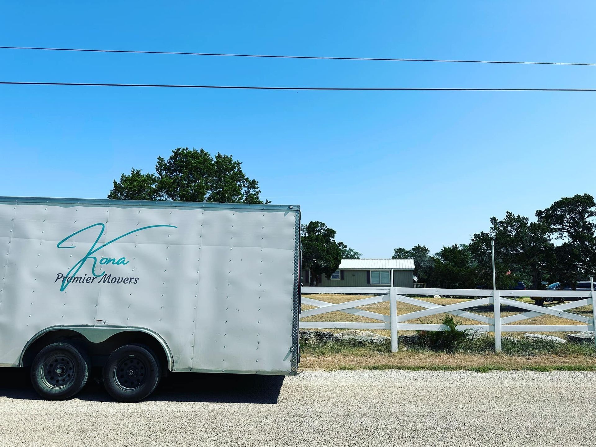 A white trailer is parked on the side of the road next to a white fence.