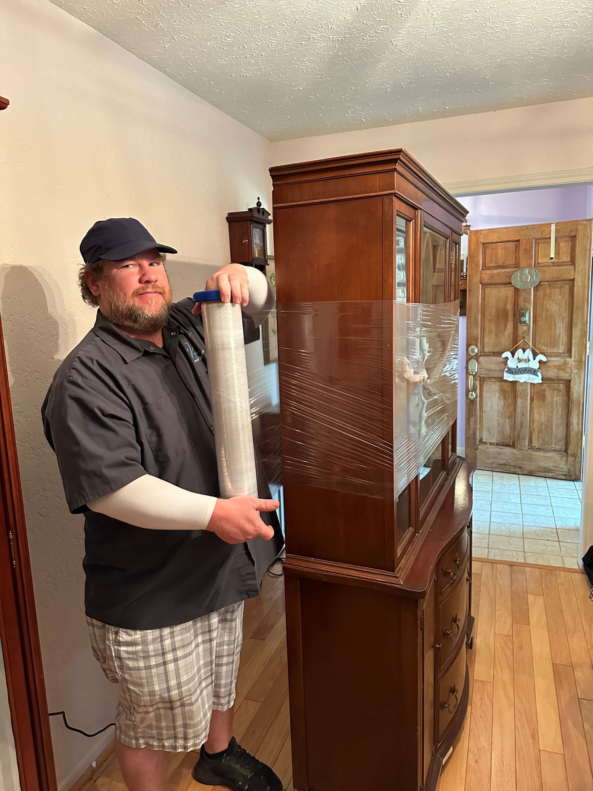Man wrapping a tall wooden cabinet in protective foam in a home hallway
